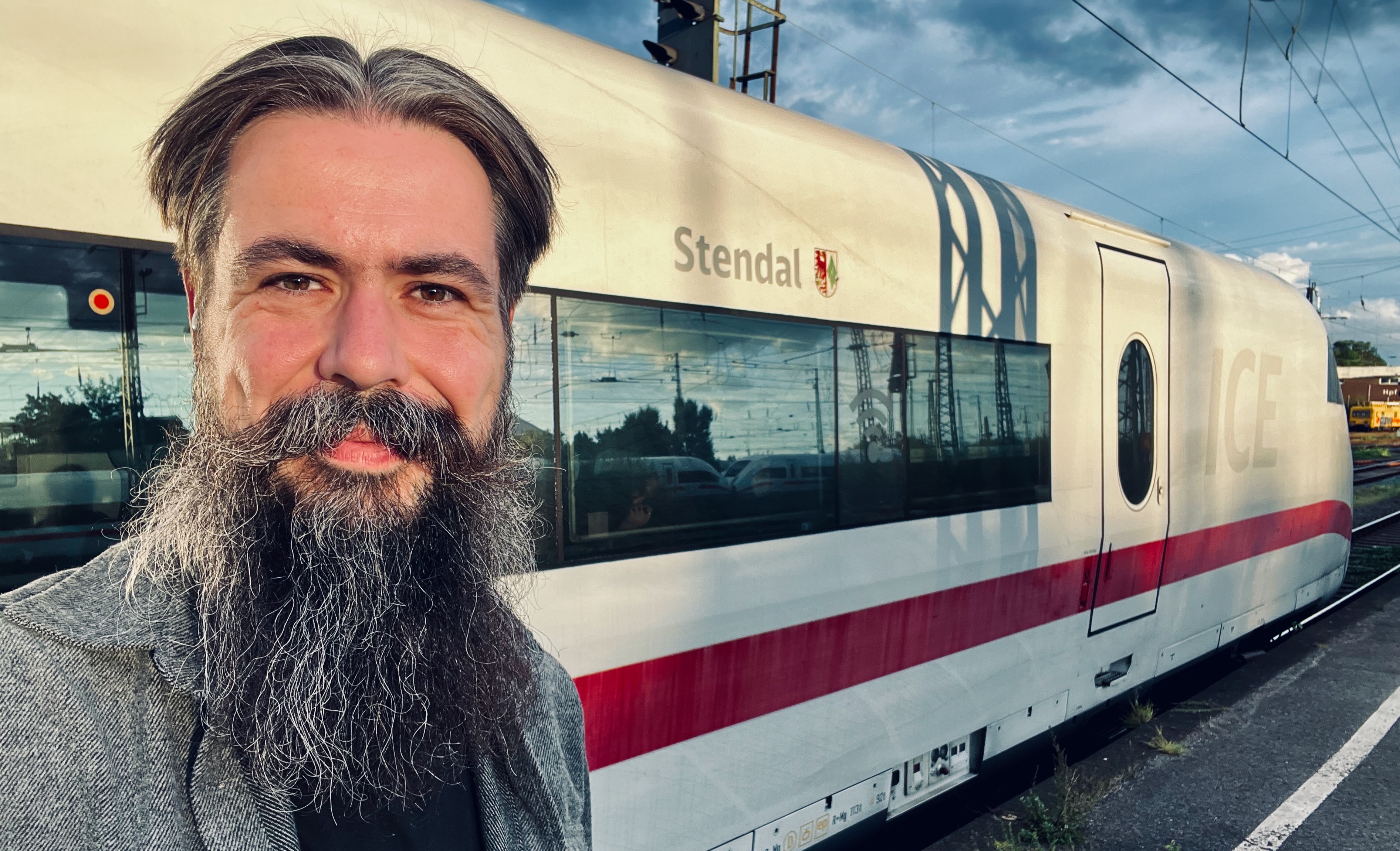 Selfie von Tobias Kremkau am Bahnhof Stendal vor einem weißen ICE mit rotem Streifen und der Aufschrift „Stendal“.